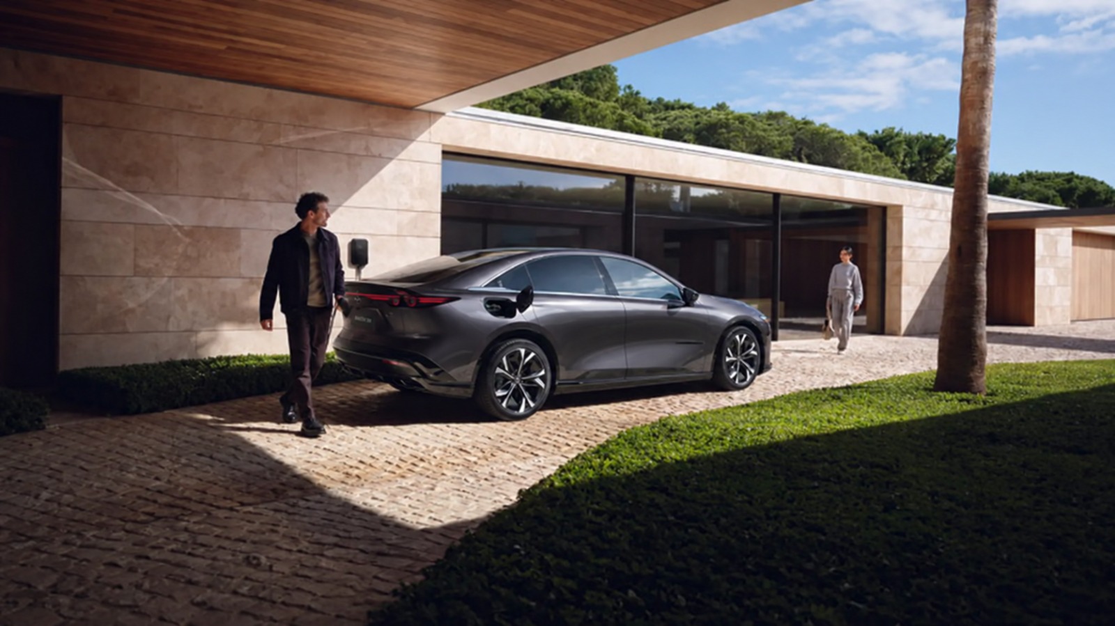 Grijze elektrische sedan voor een modern huis met laadpunt aan de gevel